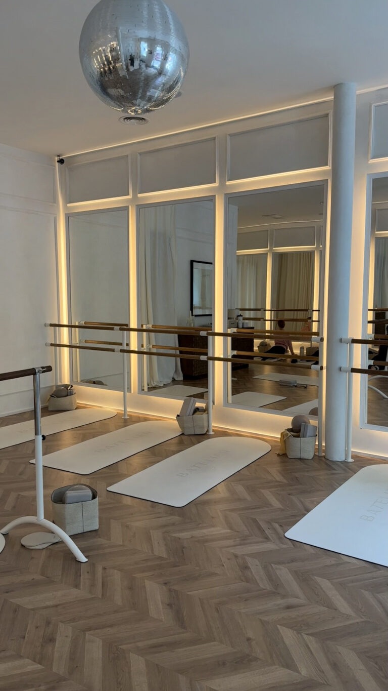 A bright Pilates studio with mirrored walls, ballet barres, yoga mats, and a disco ball hanging from the ceiling.